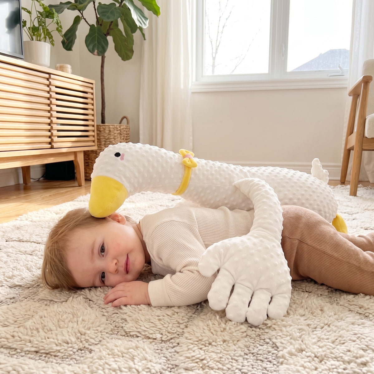 Toddler settling calmly on a rug hugging the Momi Toys weighted duck plush with its long arms wrapped around