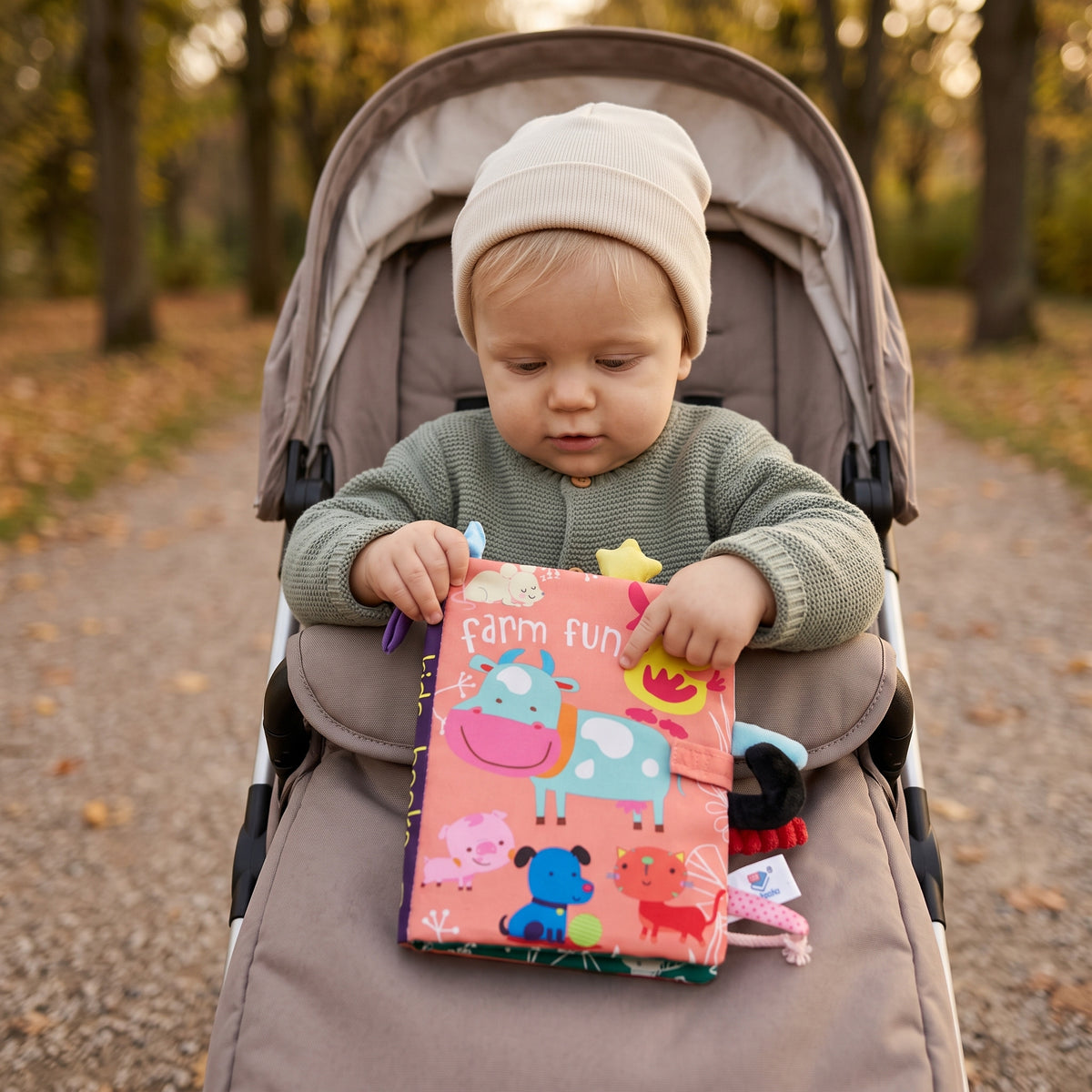 Baby holding the Momi Toys Soft Cloth Book, Farm, in a stroller