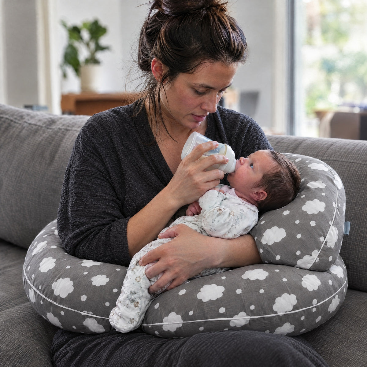 Mom bottle-feeding her newborn on the Momi Toys cradle nursing pillow in grey clouds print