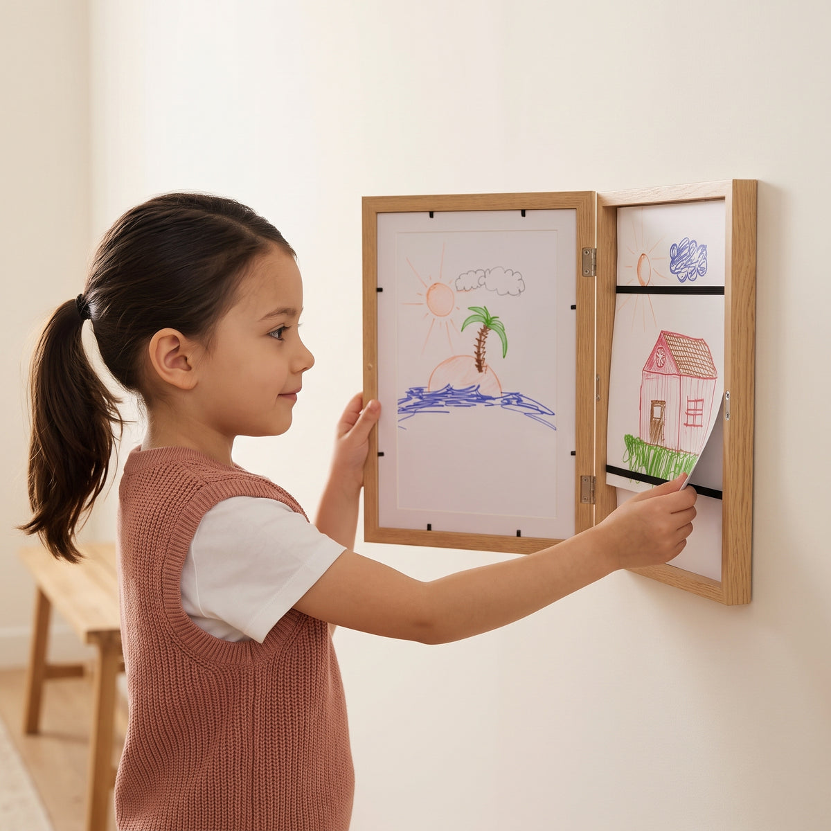 Girl adding her drawing to the Momi Toys Kids Art Display Frame, natural wood